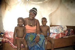 Habibatu Fugbawa sits with two of her children in front of the insecticide-treated mosquito net she received in 2010 from the United Methodist Church's Imagine No Malaria campaign at her home in Bumpe, Sierra Leone.