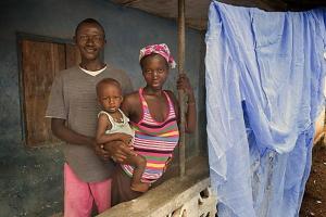 Abdul and Maseray Koroma stand with their daughter, Kelvin, 9 months, beside the new insecticide-treated mosquito net they received from the Imagine No Malaria campaign.